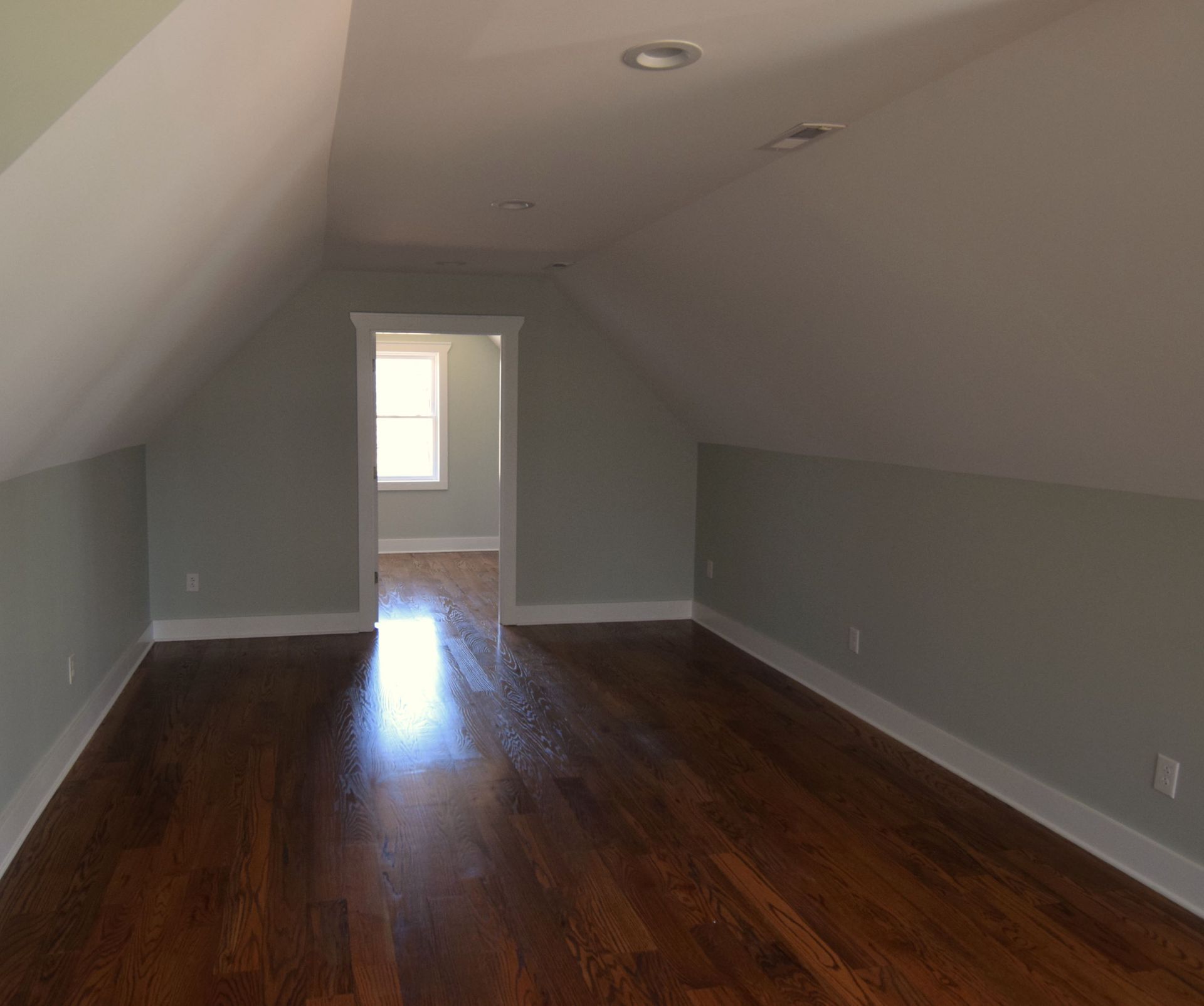 An empty attic with hardwood floors and gray walls.