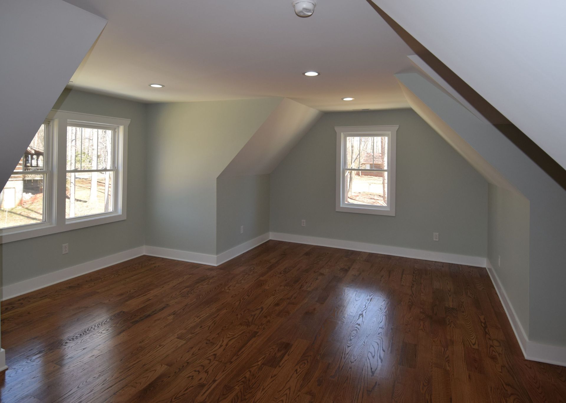 An empty room with hardwood floors and two windows