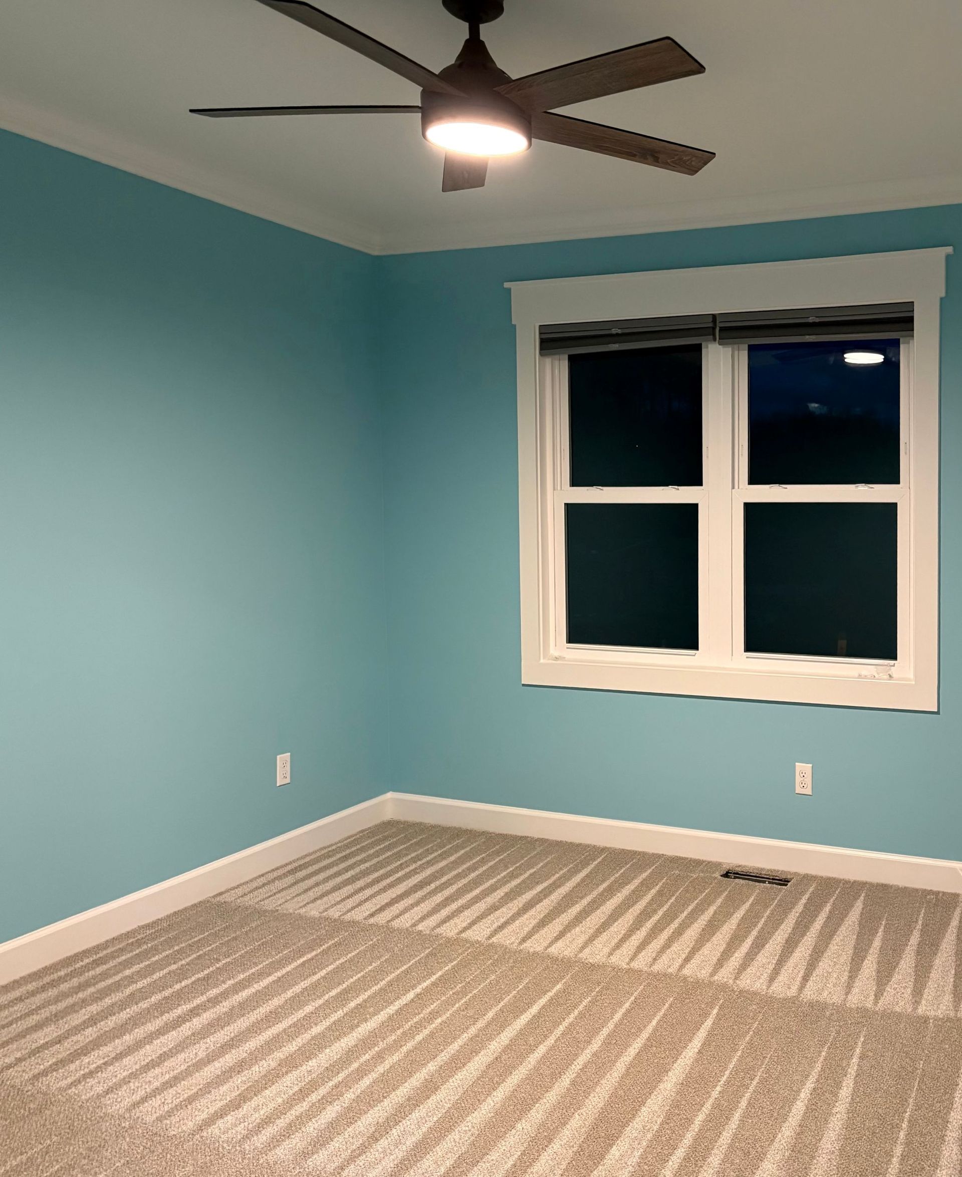 Empty room with aqua blue walls, white trim, tan carpet, and a window.
