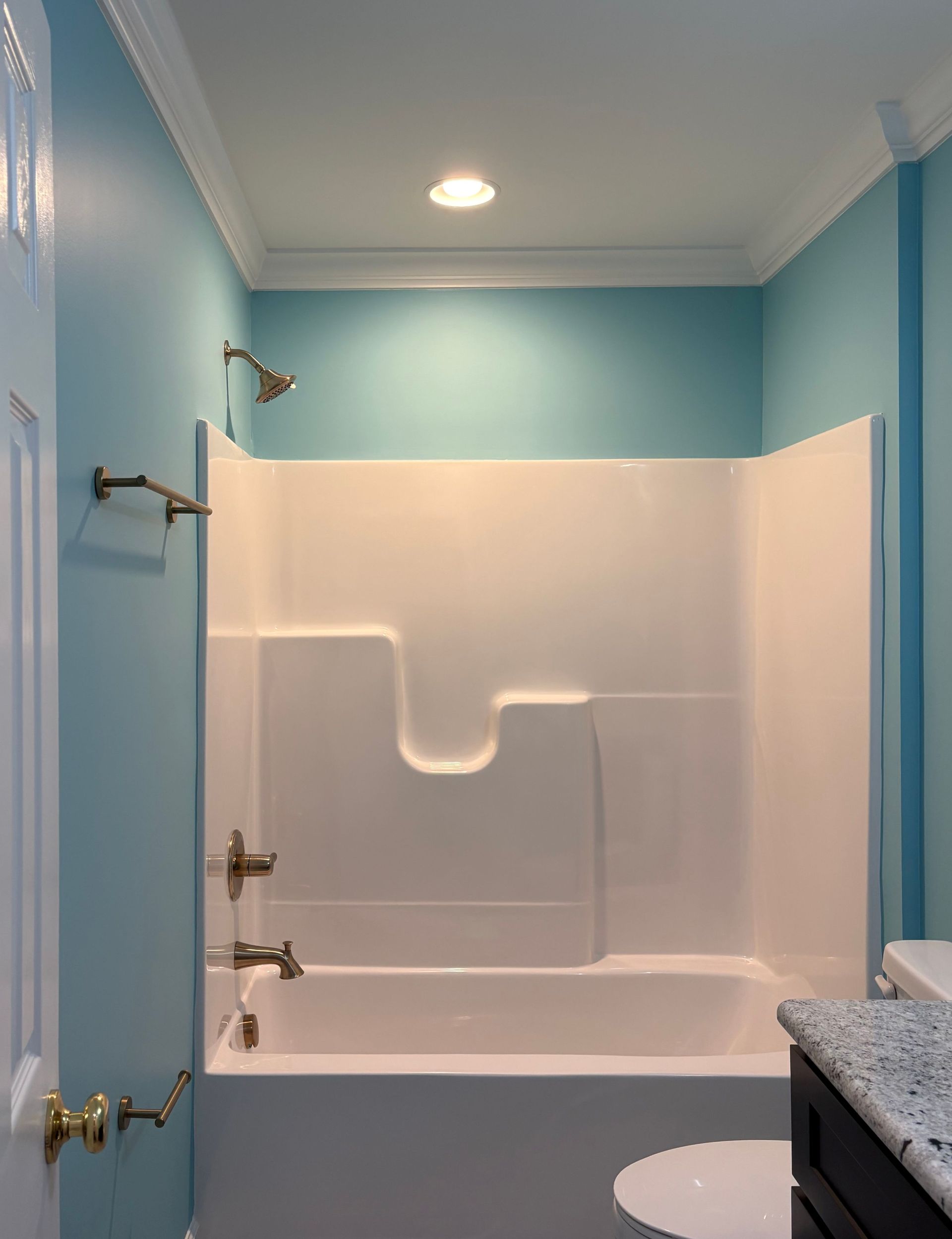 Bathroom with blue walls, white tub/shower surround, gold fixtures, and a toilet.