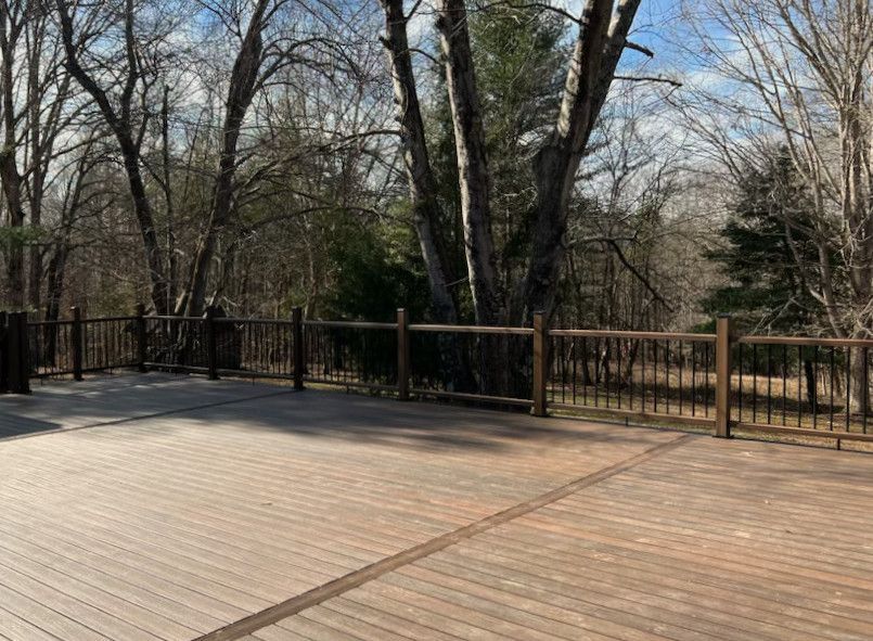 Wooden deck with railing overlooking a wooded area with bare trees.