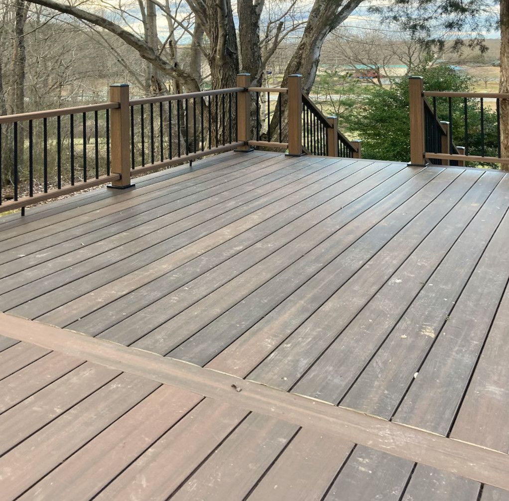 Deck with brown composite boards, black railing, and a view of trees and fields.