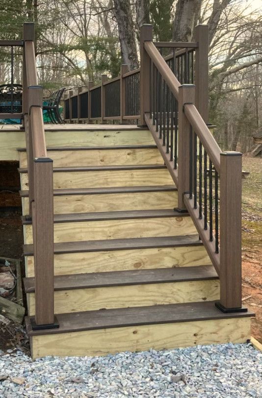 Wooden outdoor stairs with brown railing and black metal spindles.