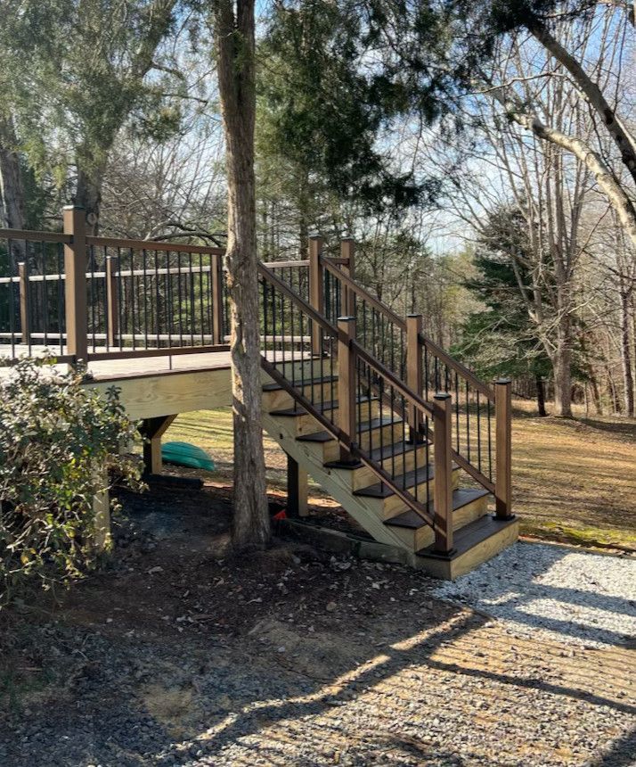 Wooden deck with stairs, built around a tree. Brown railing and steps. Gravel path in foreground.