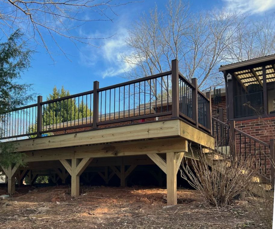 Newly built wooden deck with dark brown railing and supports, set against a blue sky with bare trees.