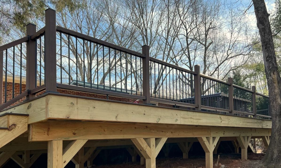 Wooden deck with dark brown railing and vertical black bars, supported by wooden beams.