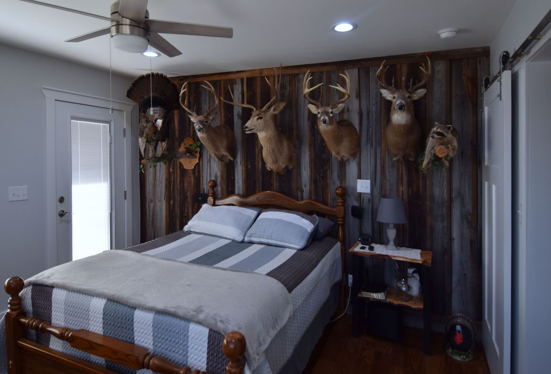 A bedroom with a bed , nightstand , ceiling fan , and deer heads hanging on the wall.