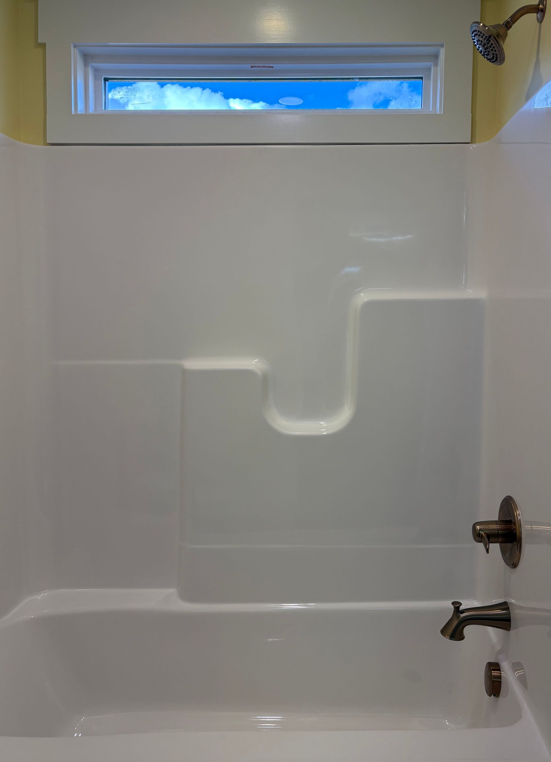 White bathtub with shower surround, window above.