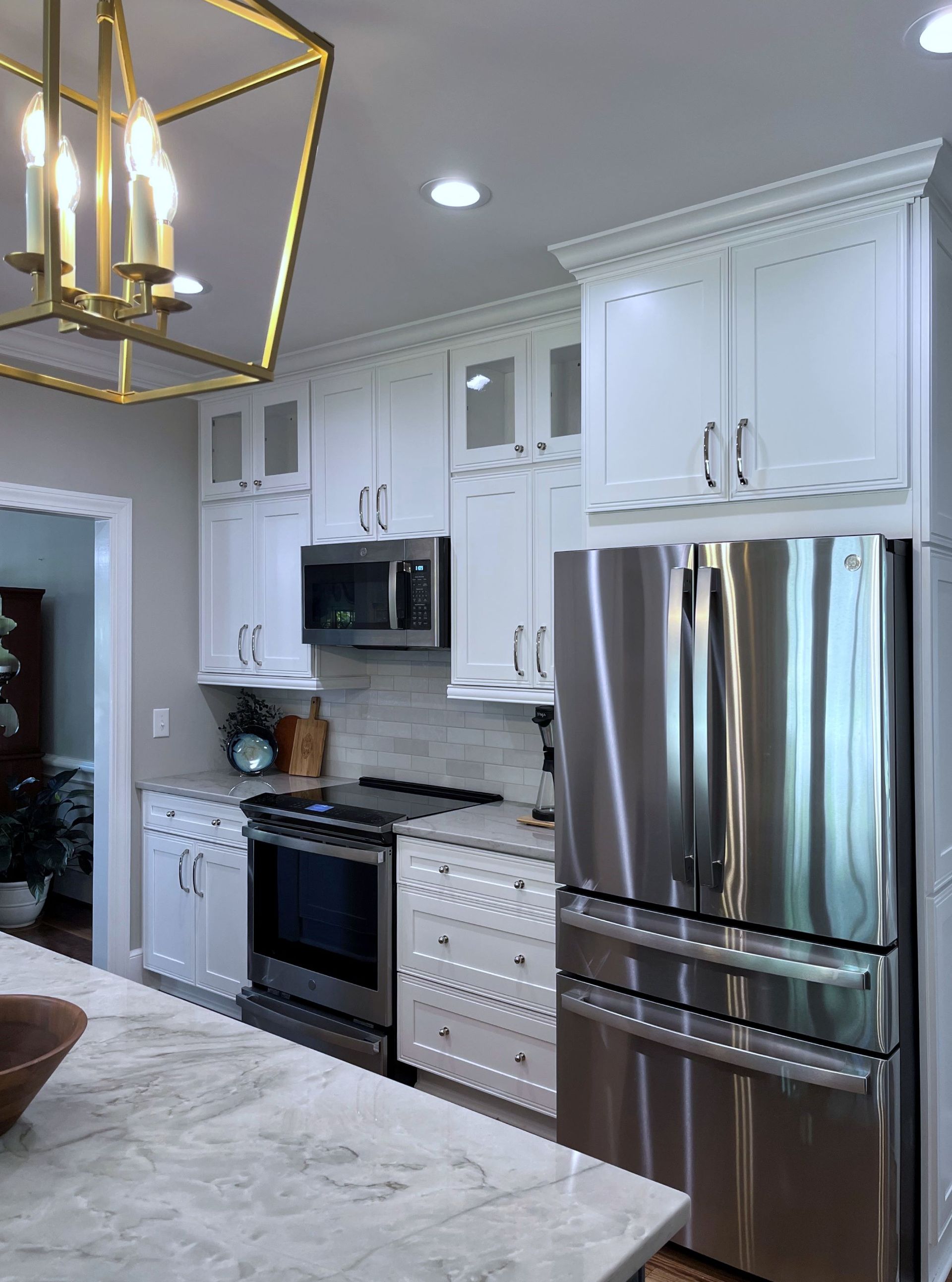 White kitchen with stainless steel appliances and gold chandelier.