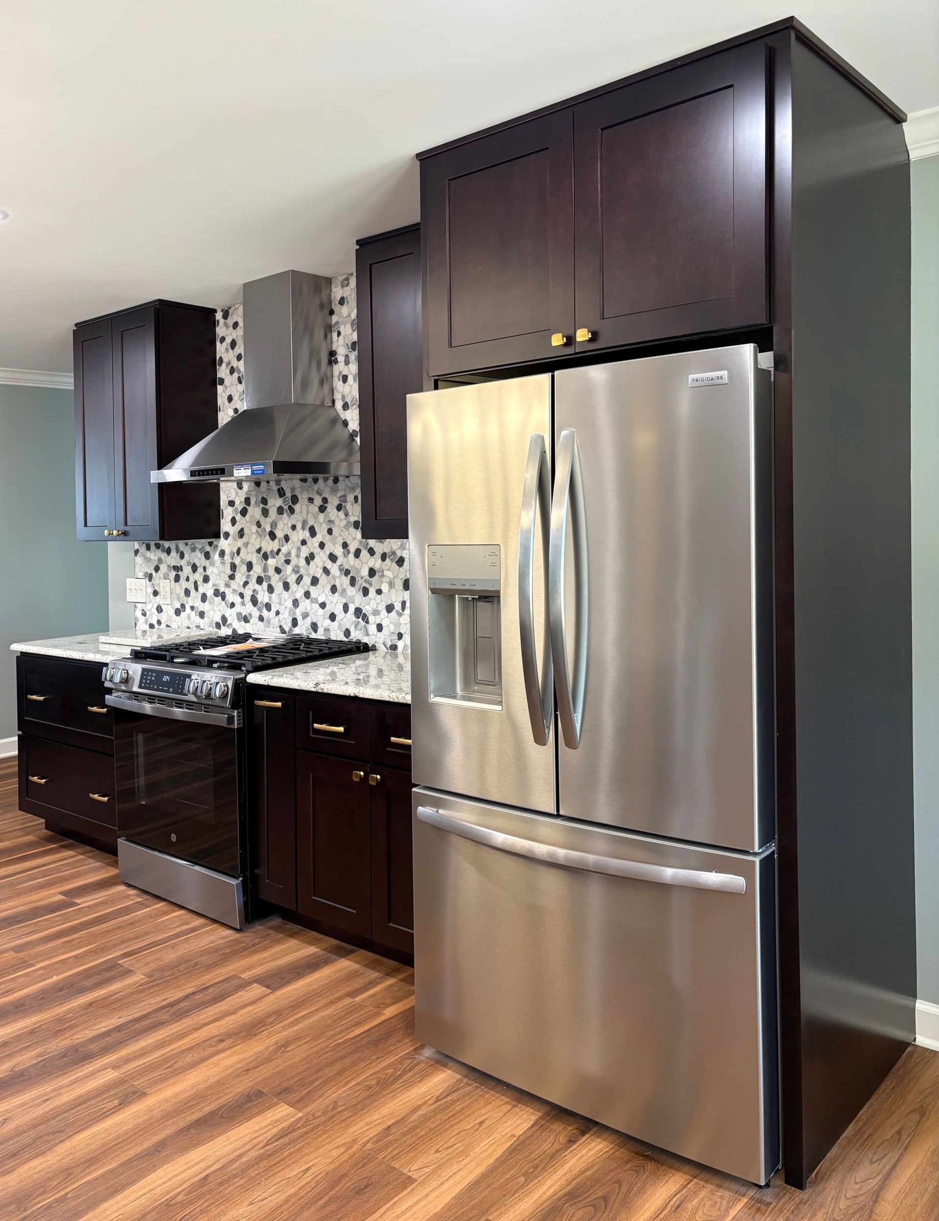 Kitchen with stainless steel refrigerator and dark wood cabinets; granite countertops, stove, and hood.