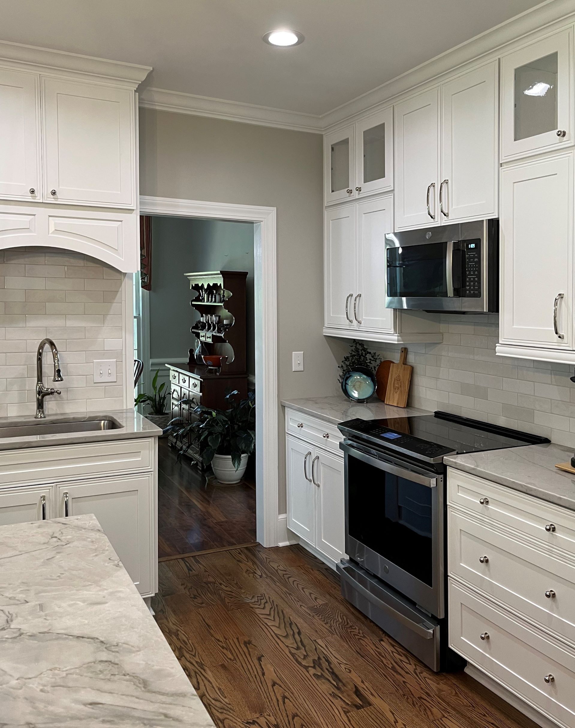White kitchen with stainless steel appliances, marble countertops, and a view into another room.