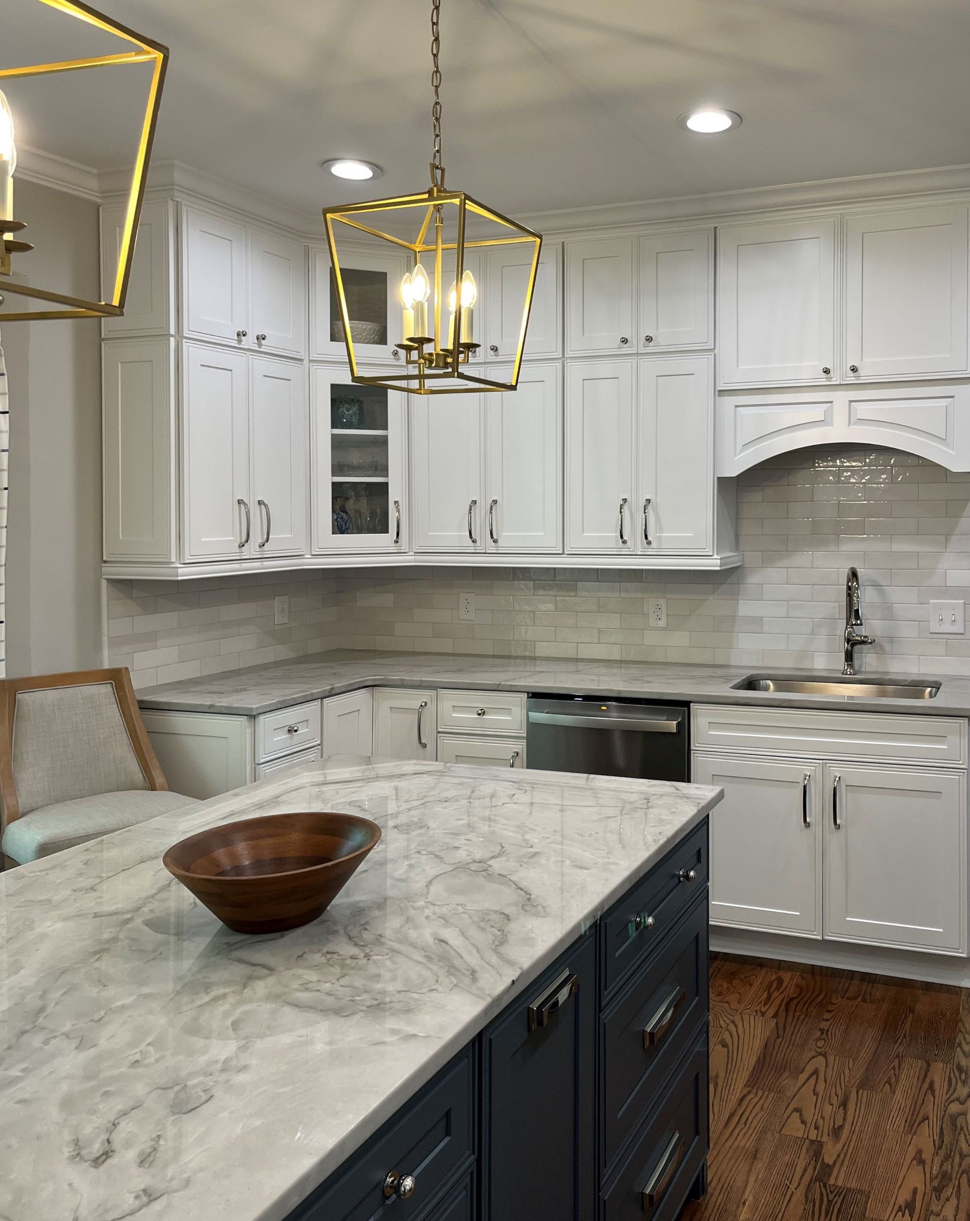 White kitchen with a blue island, marble countertops, and gold pendant lights.