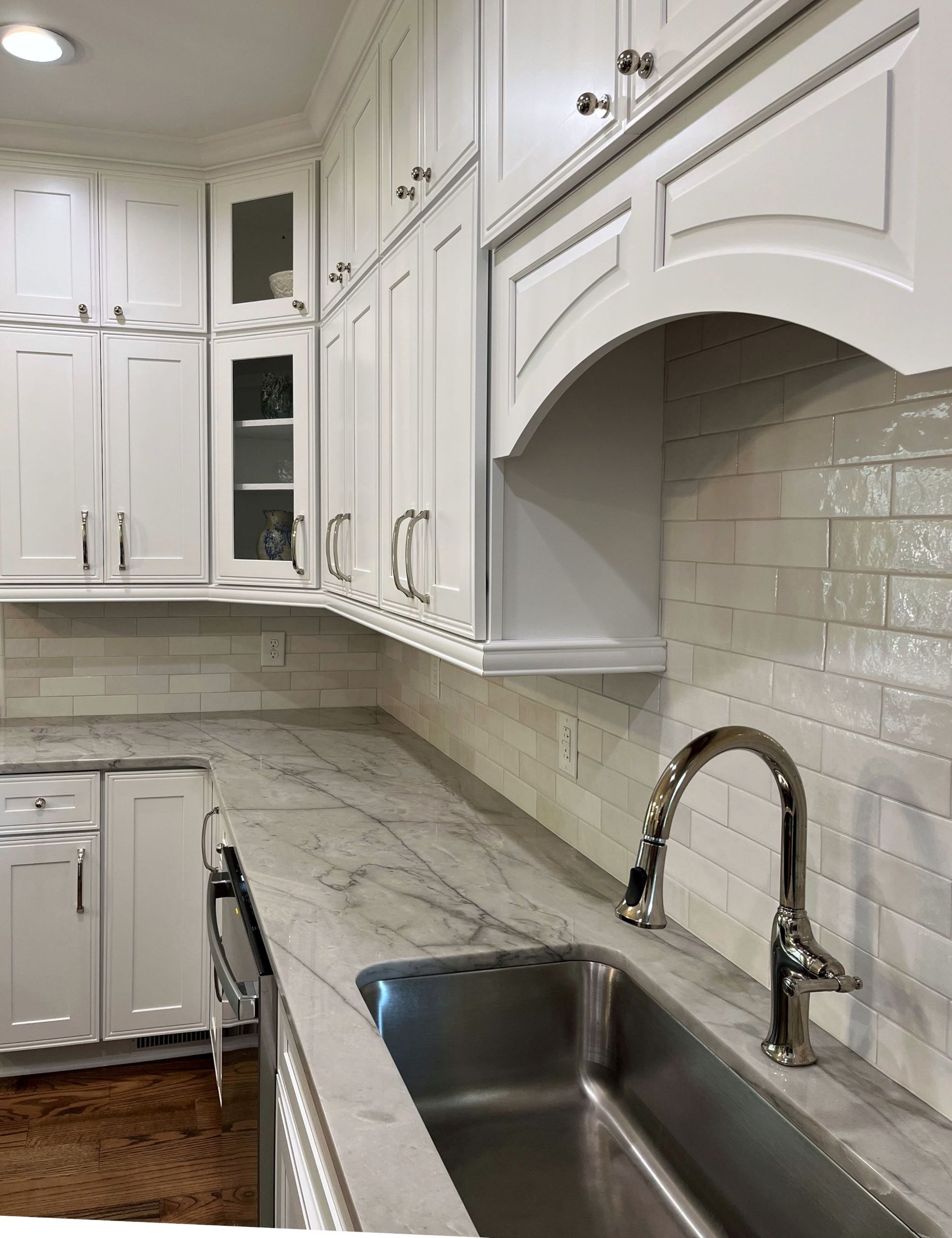 White kitchen with marble countertop, stainless steel sink, and white cabinets.