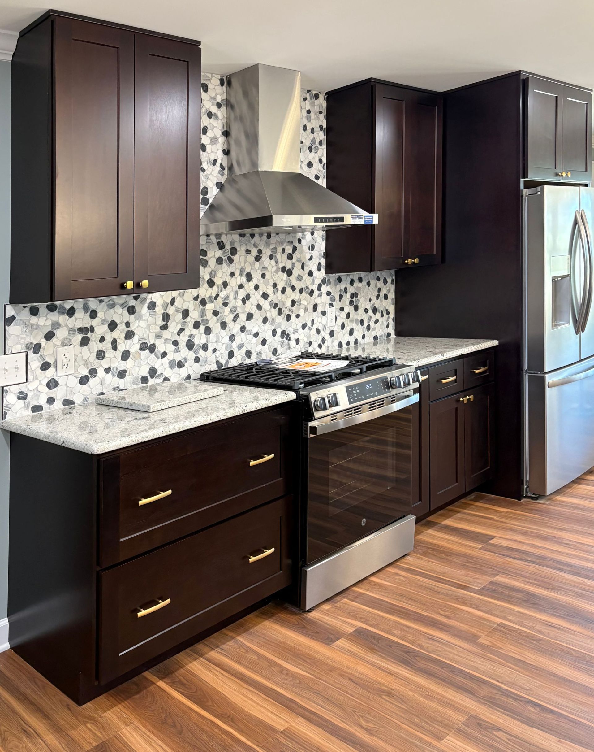 Dark brown kitchen cabinets with stainless steel appliances, white countertops, and a mosaic backsplash.