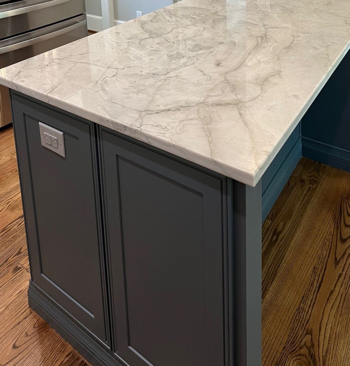Kitchen island with a marble countertop and dark blue cabinets. Wooden floor.