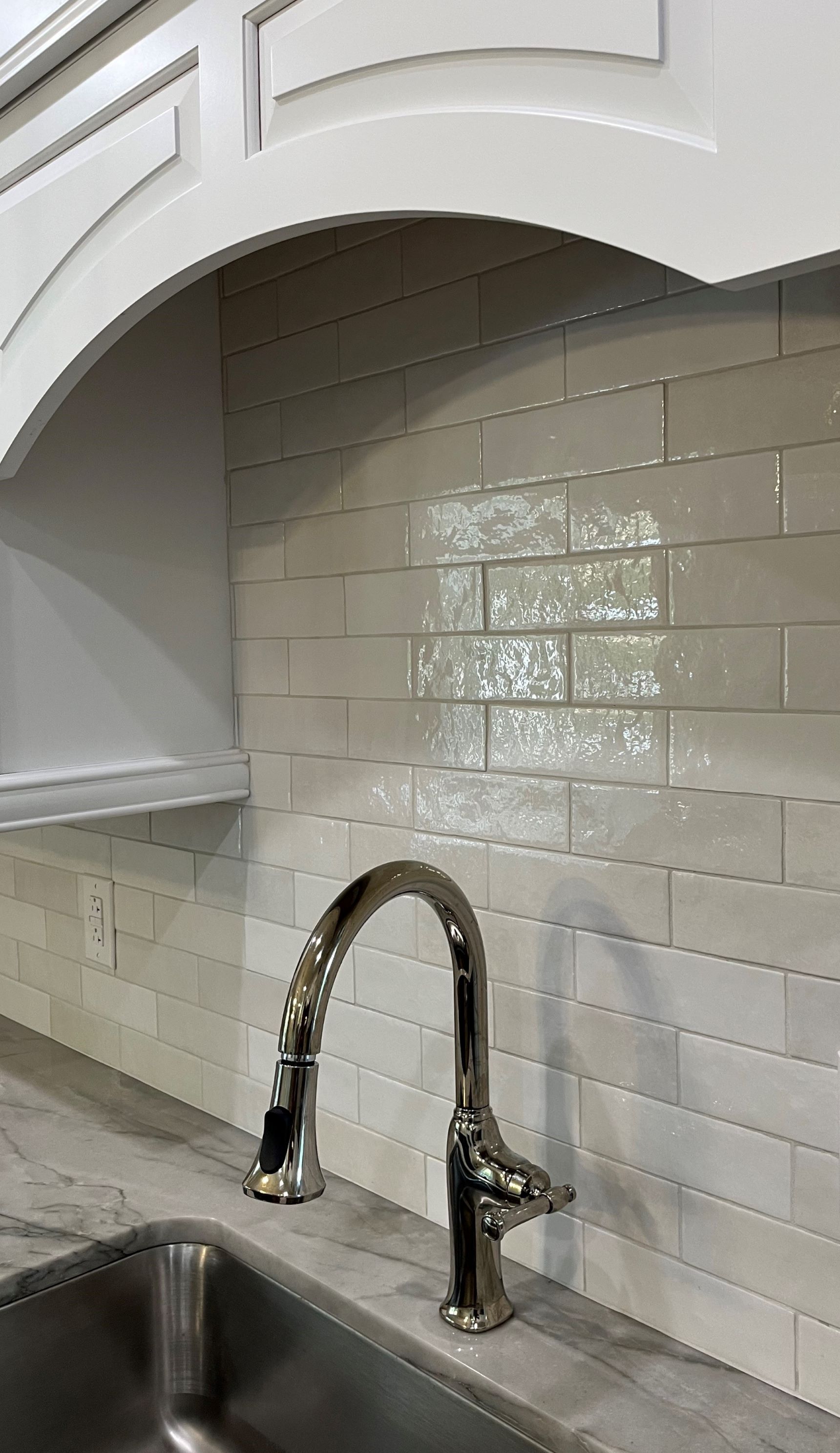 Stainless steel kitchen faucet against light gray subway tile backsplash and white cabinets.