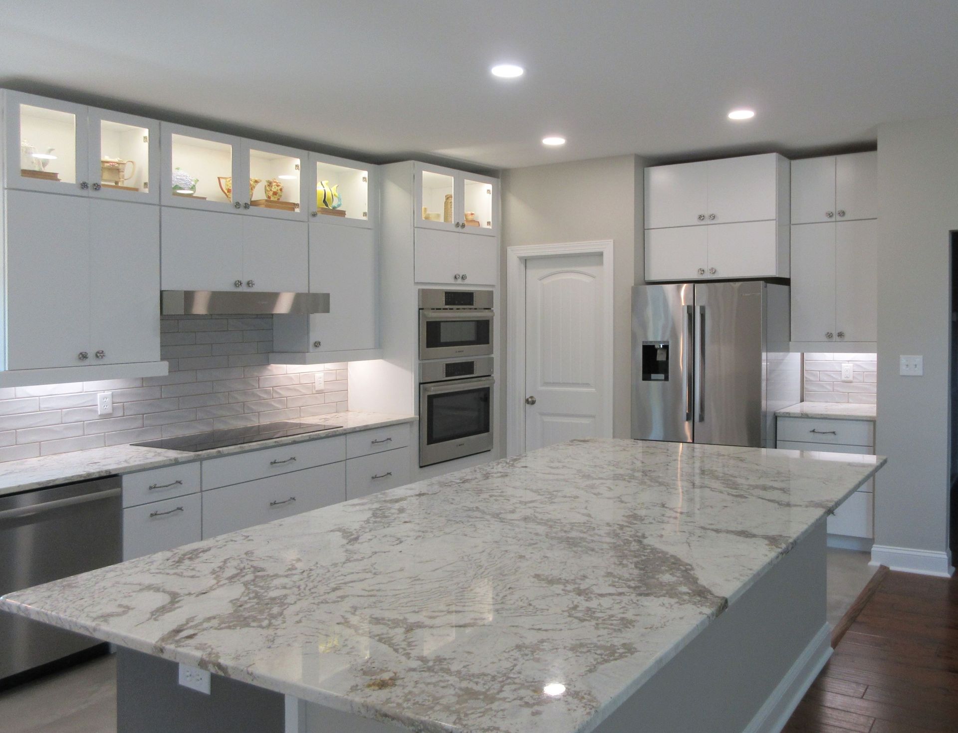 Modern white kitchen with stainless steel appliances, granite countertops, and a large island.