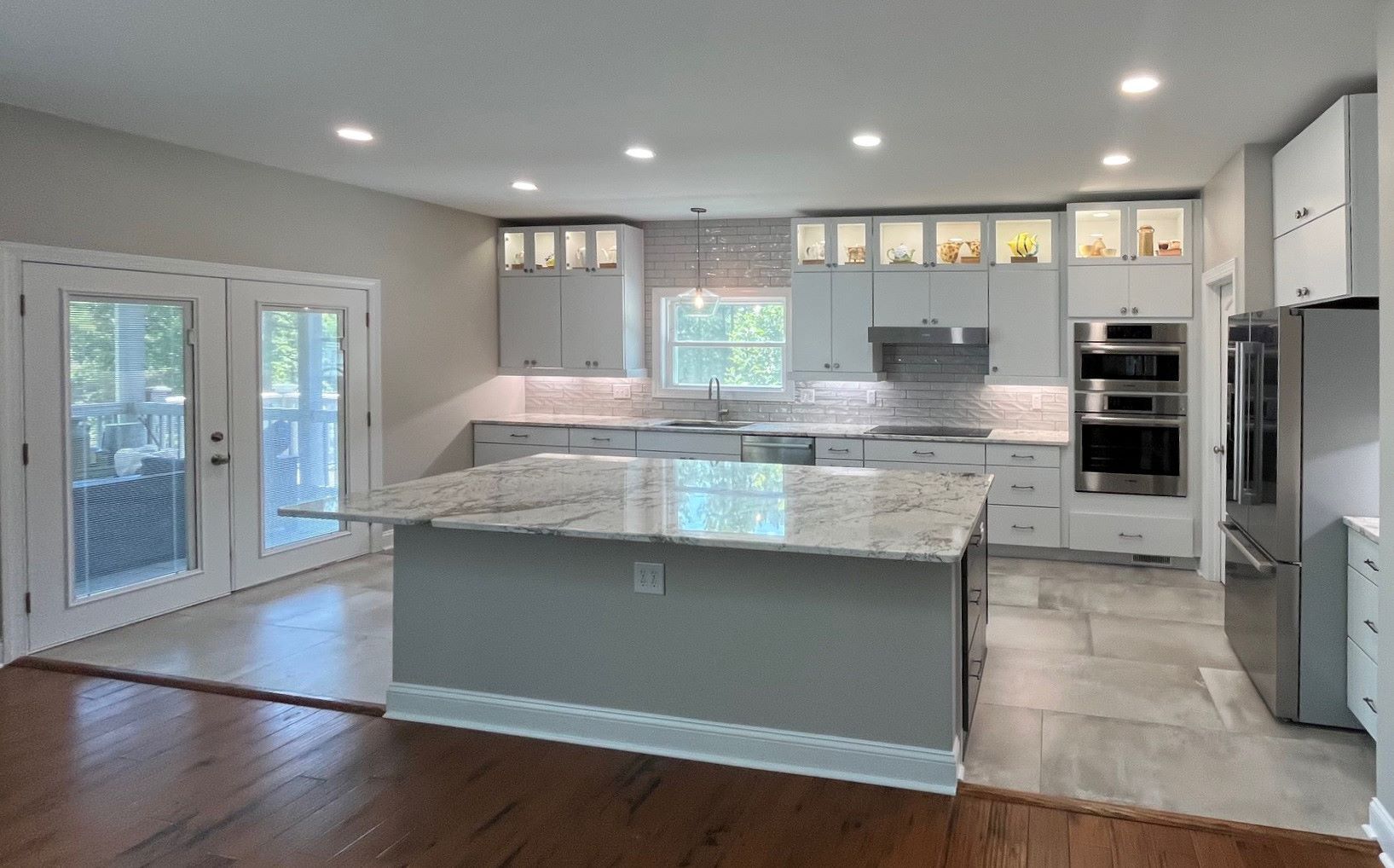 Modern kitchen with light gray cabinets, granite island, stainless steel appliances, and French doors.