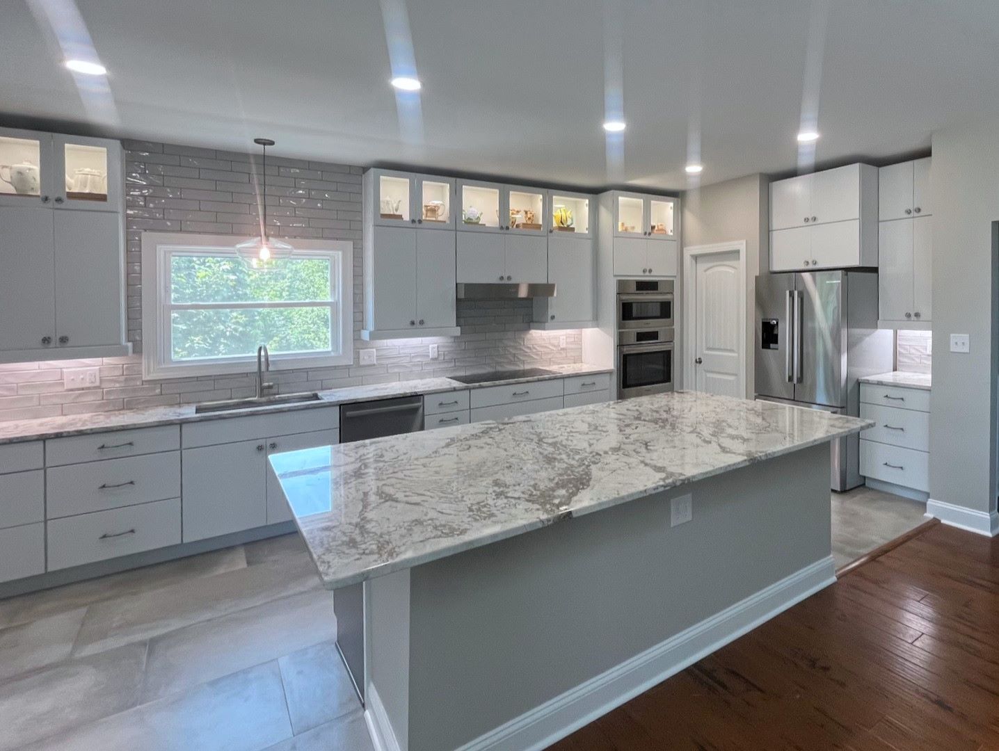 Modern kitchen with gray cabinets, marble countertops, island, and stainless steel appliances.