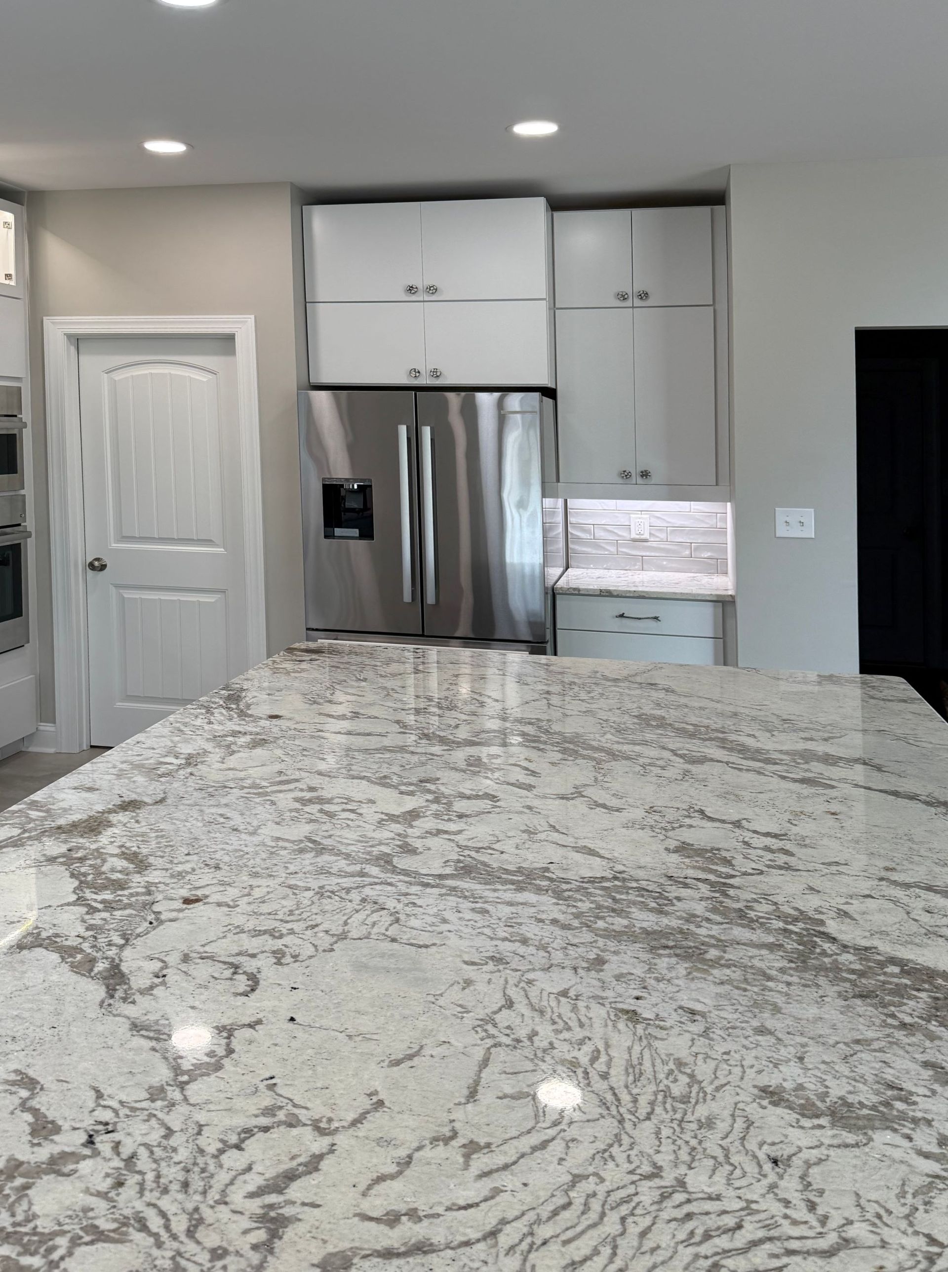 Kitchen with a granite countertop island, white cabinets, stainless steel refrigerator.