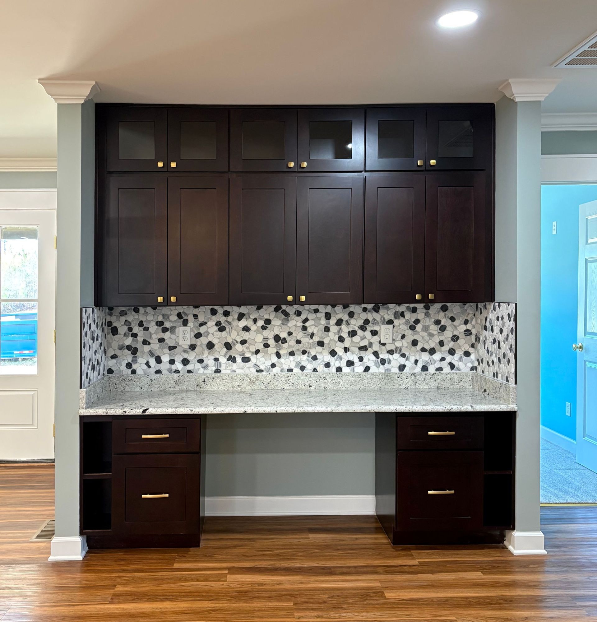 Dark brown built-in desk with cabinets, granite countertop, and mosaic backsplash.