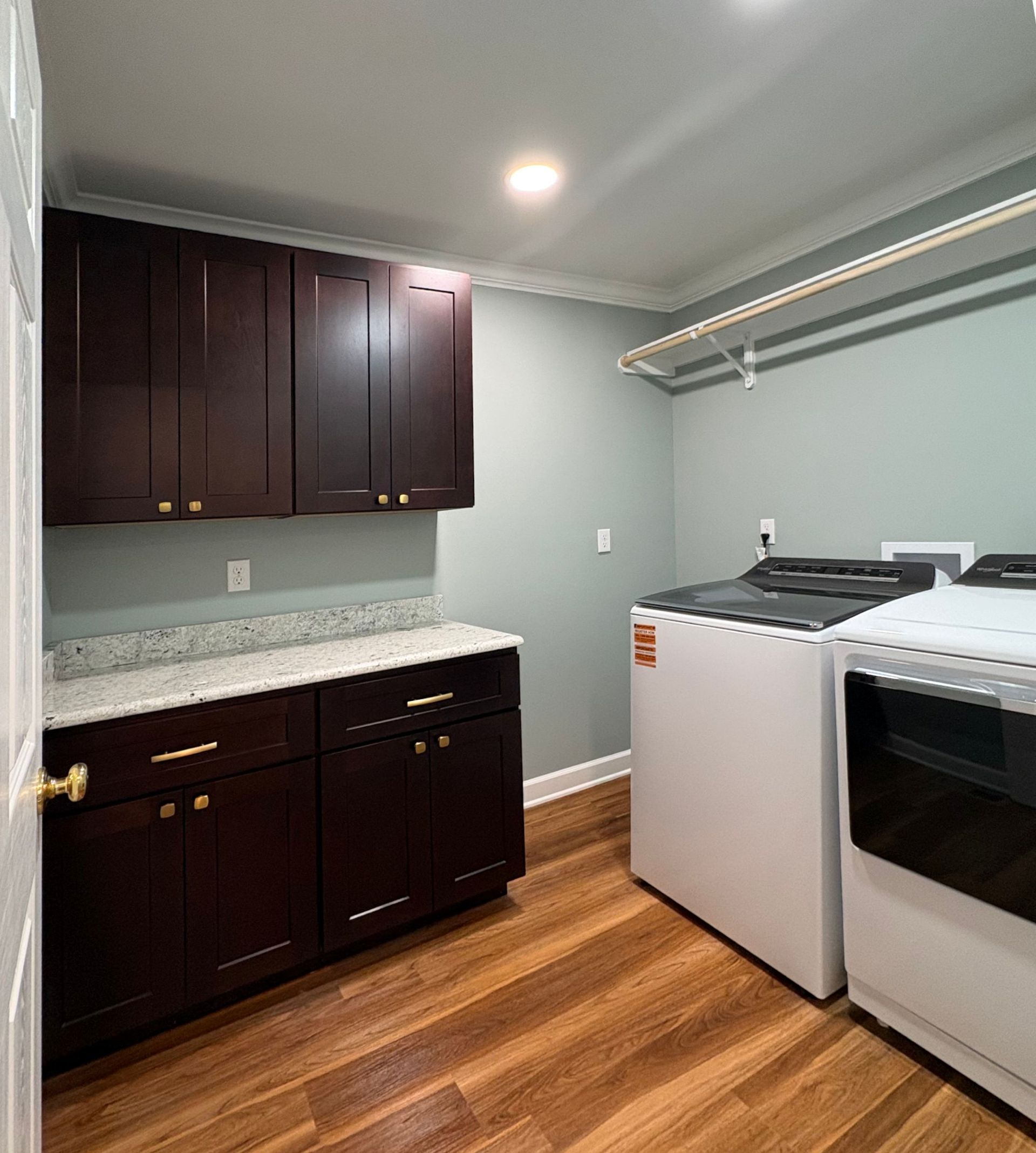 Laundry room with dark cabinets, white appliances, and wood flooring.
