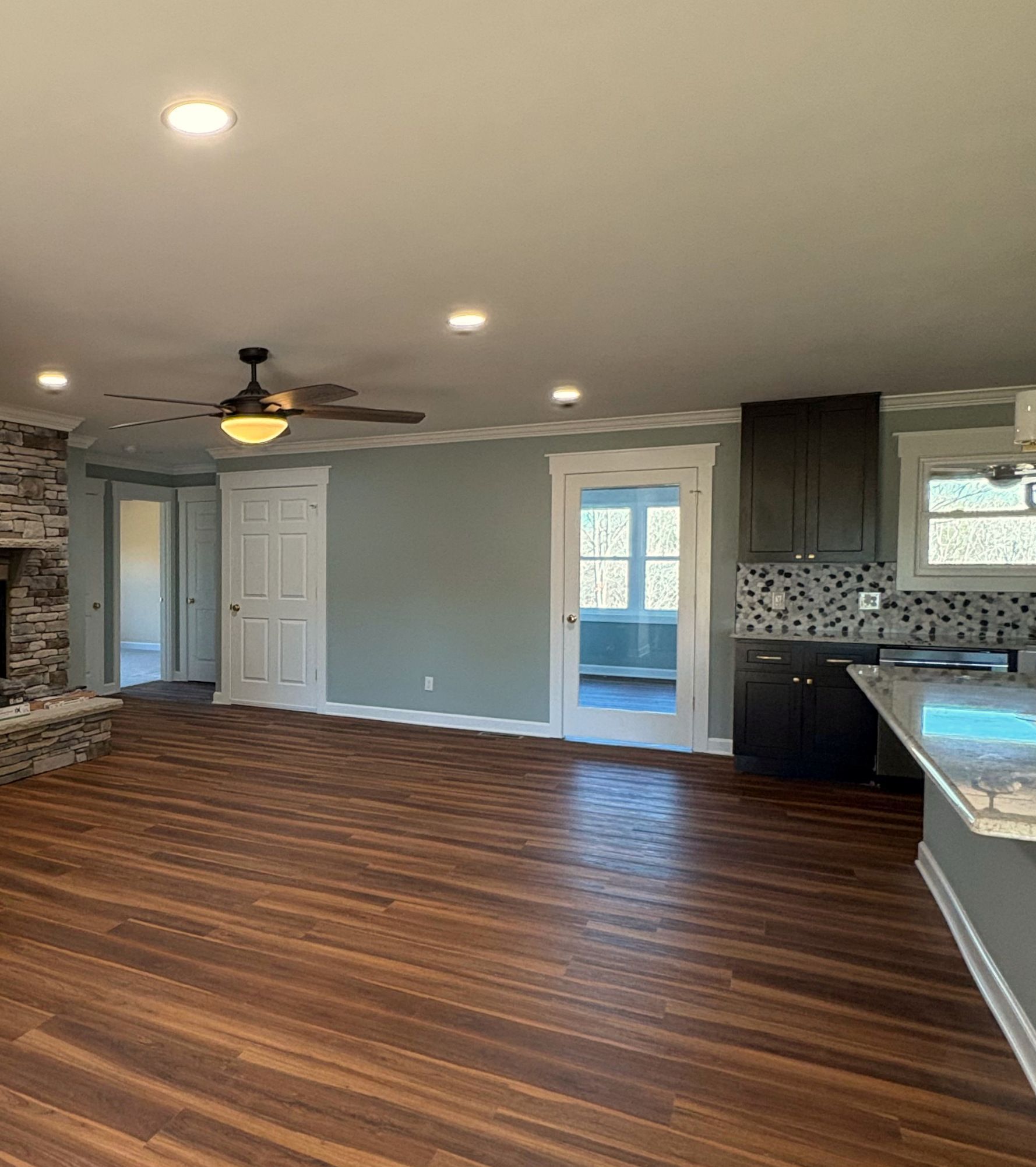 Spacious open-concept living space with hardwood floors, a kitchen with dark cabinets, and a stone fireplace.