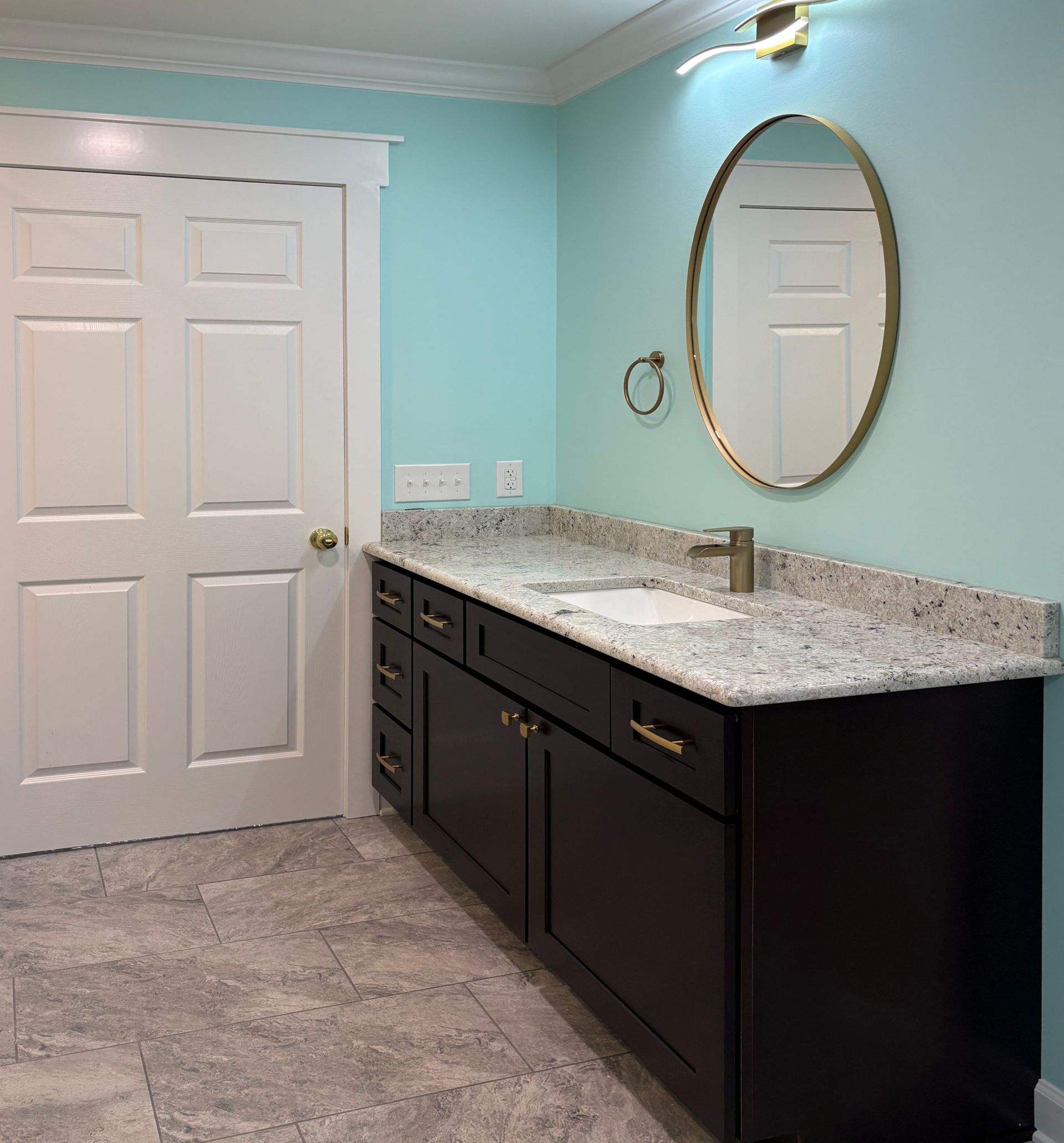 Bathroom with dark cabinets, light granite countertop, oval mirror, and turquoise walls.