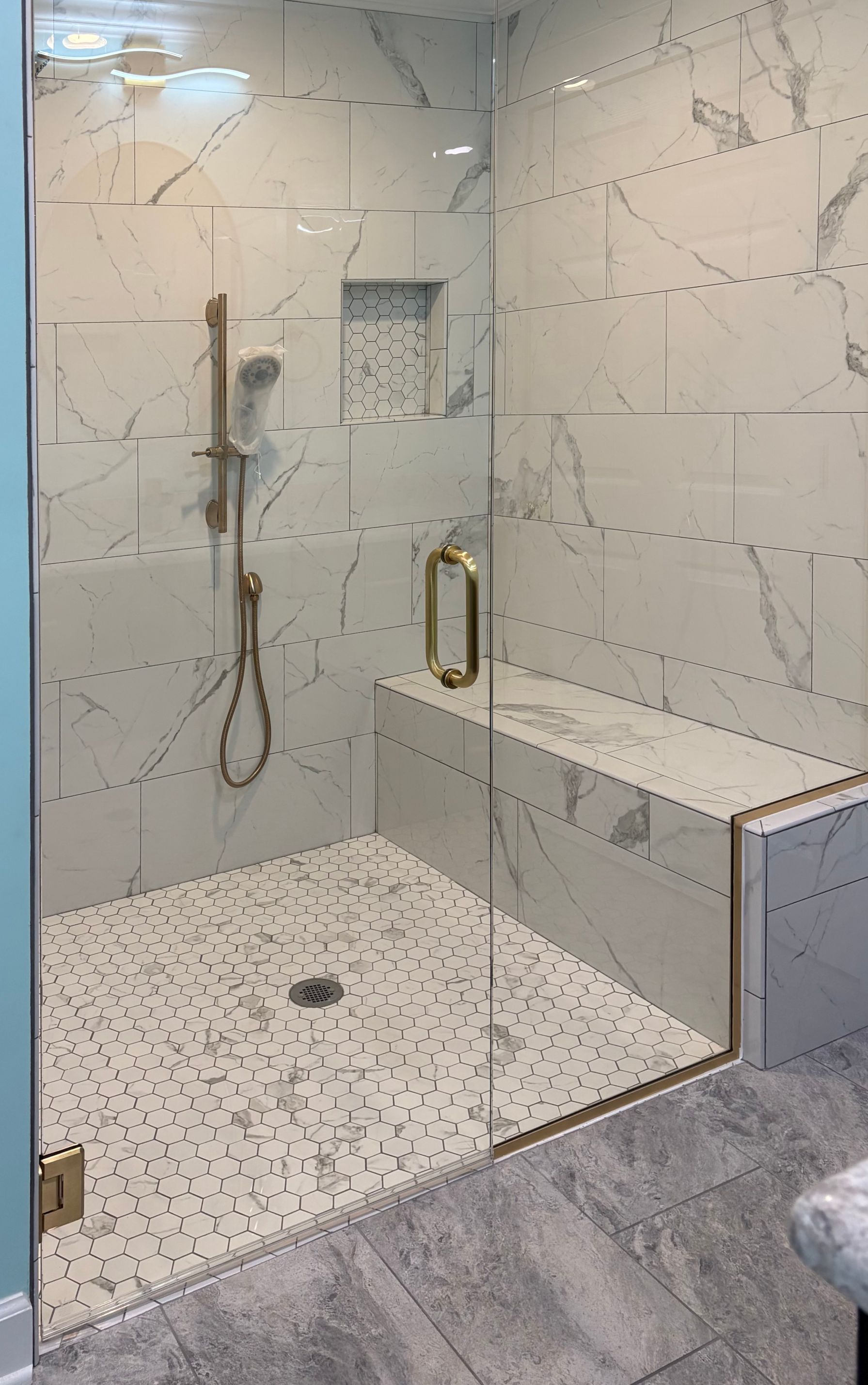Modern shower with white marble-look tiles, glass door, built-in bench, and gold hardware.