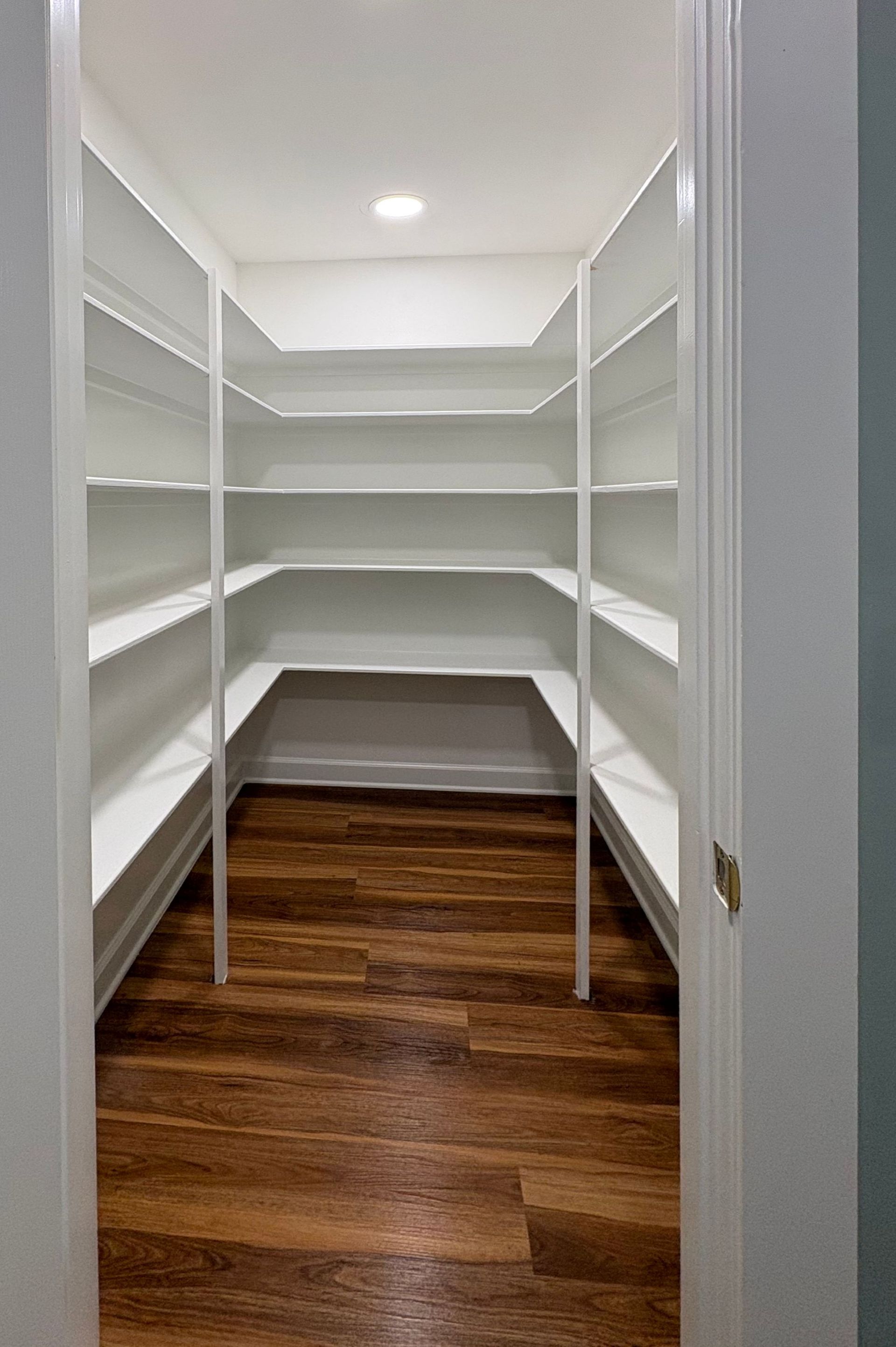 Empty white pantry with wooden floor and built-in shelving.