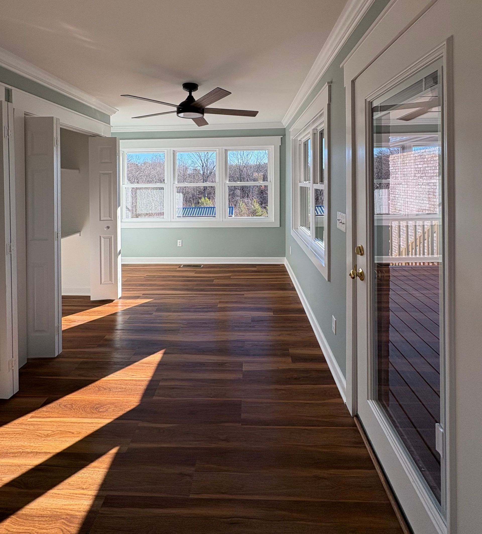Sunroom interior with hardwood floors, windows, and a ceiling fan; door to the right.
