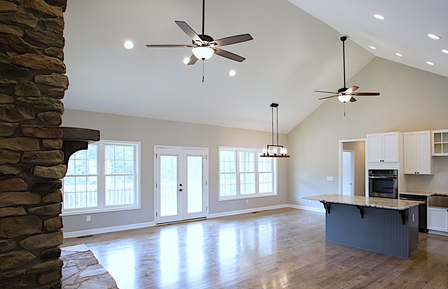 A large empty room with a ceiling fan and a kitchen.