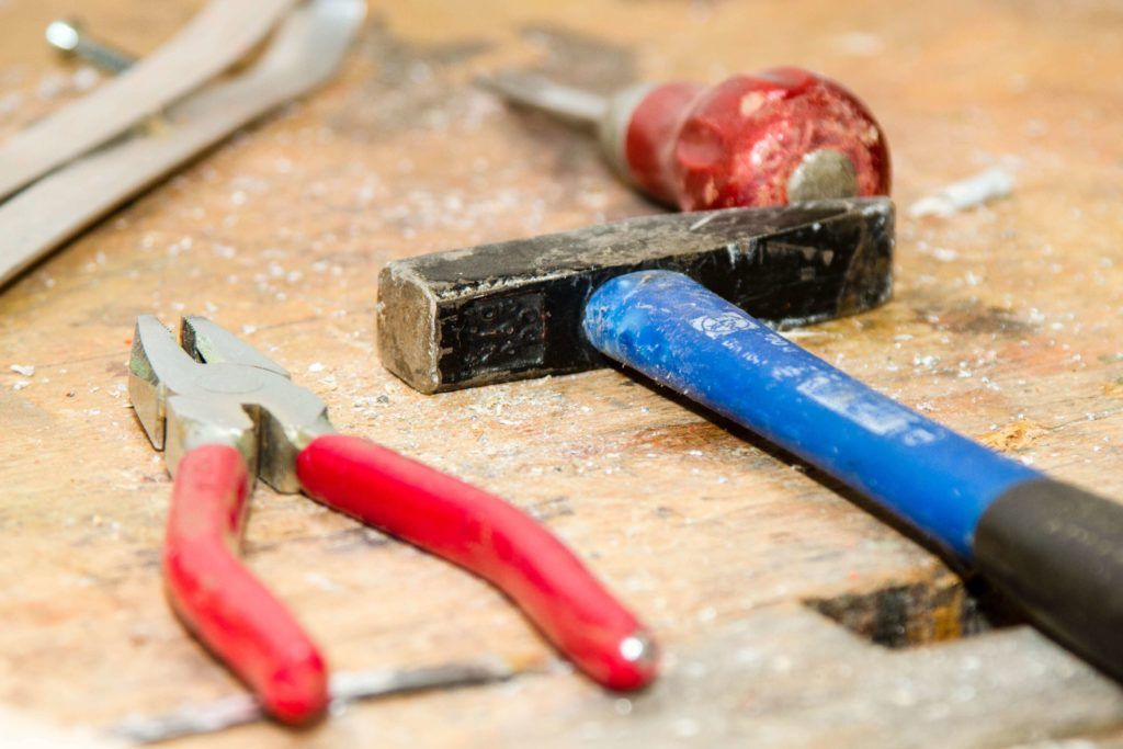 A hammer , pliers , and screwdriver are on a wooden table.