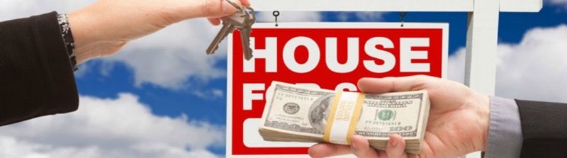 A person is holding a stack of money in front of a house for sale sign.