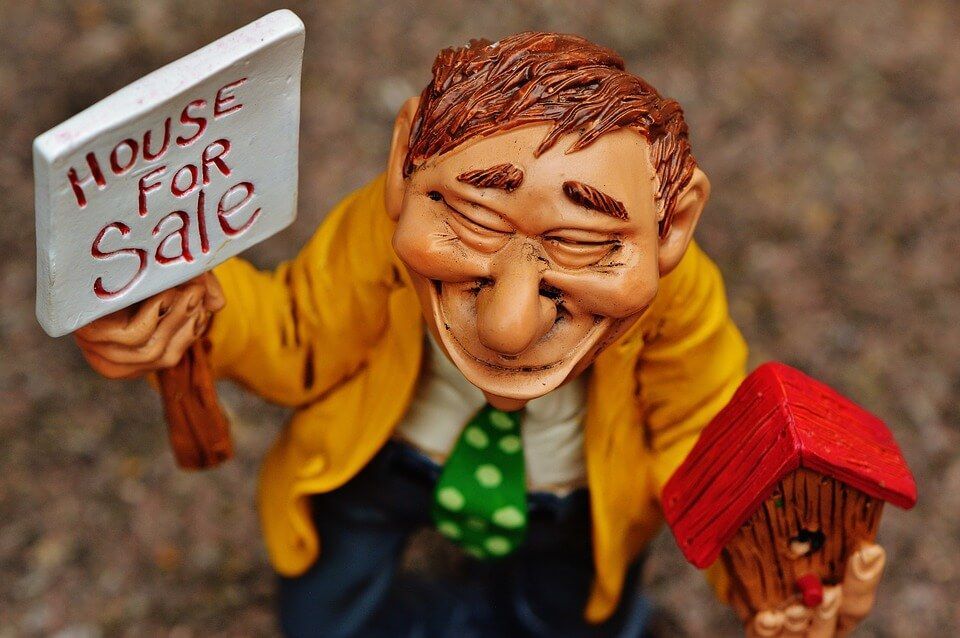 A figurine of a man holding a house for sale sign.