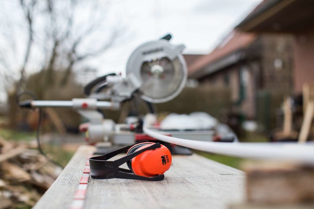A pair of ear muffs is sitting on a wooden table next to a circular saw.