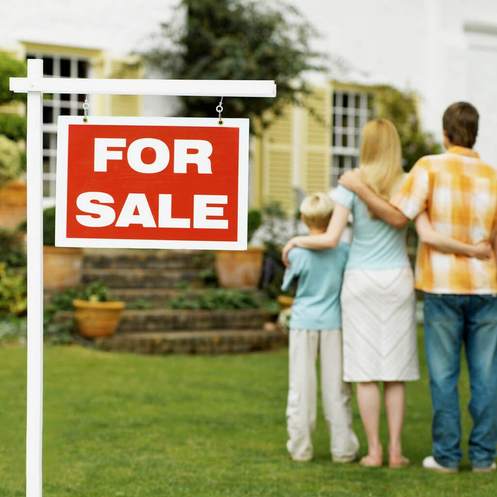 A family stands in front of a for sale sign