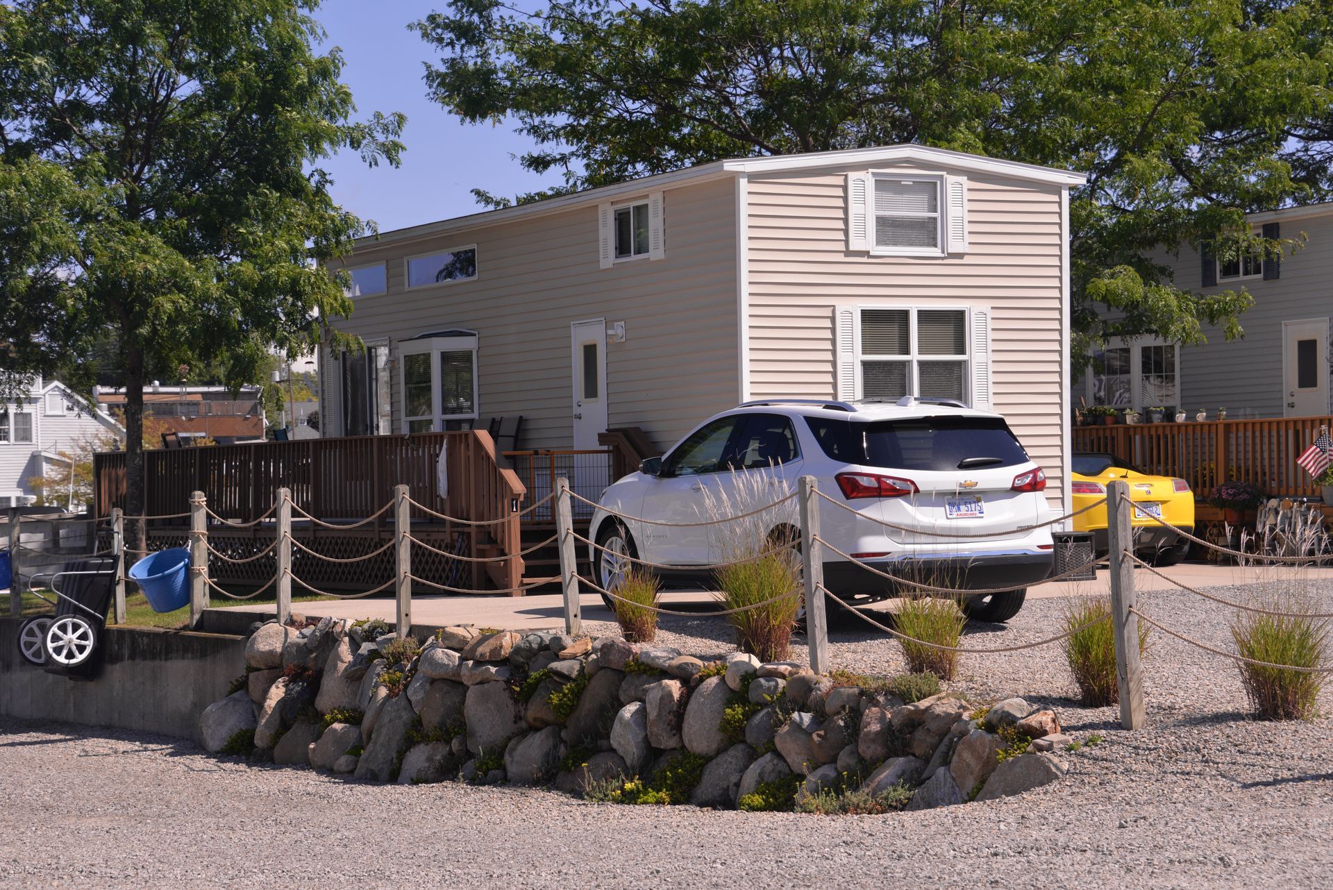 Mobile home with a white SUV parked in front, beside a rock-lined yard and trees.