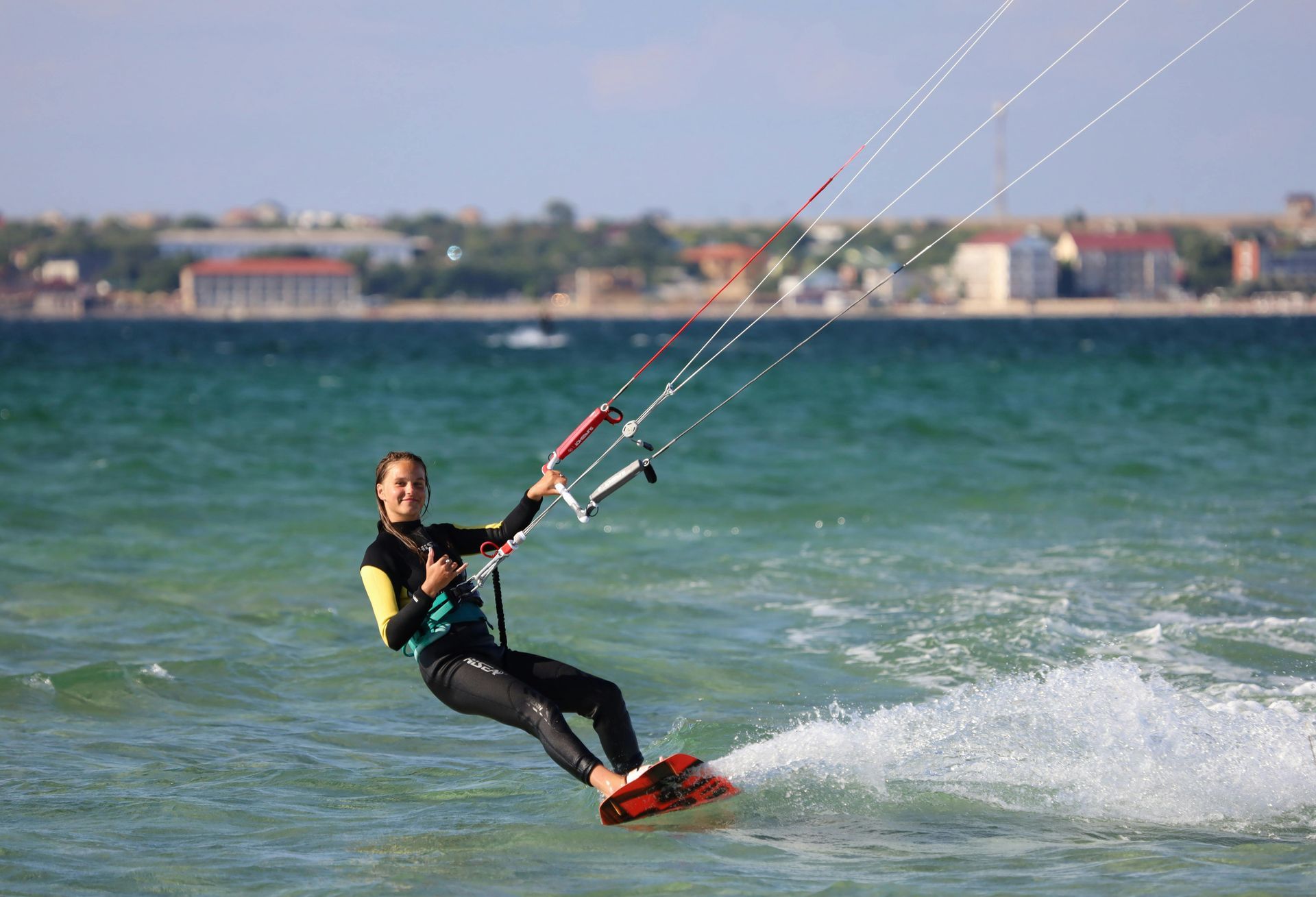 Kite surfer in a black wetsuit skims across choppy water with spray trailing behind.