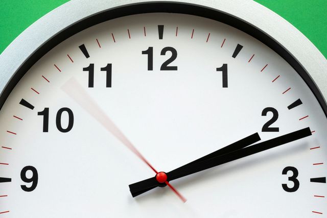 Close-up of a white analog clock showing about 2:10 with black numbers and hands.