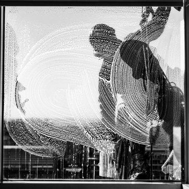 Person washing a large window with soap, creating white streaks and bubbles