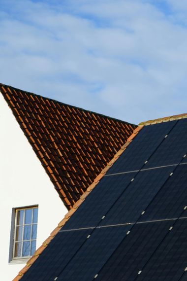 House roof with dark solar panels beside a red-tiled gable under a blue sky