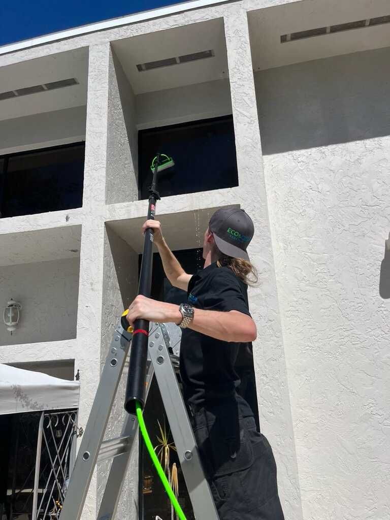 Person using a long-handled tool to clean a white building facade under a balcony opening
