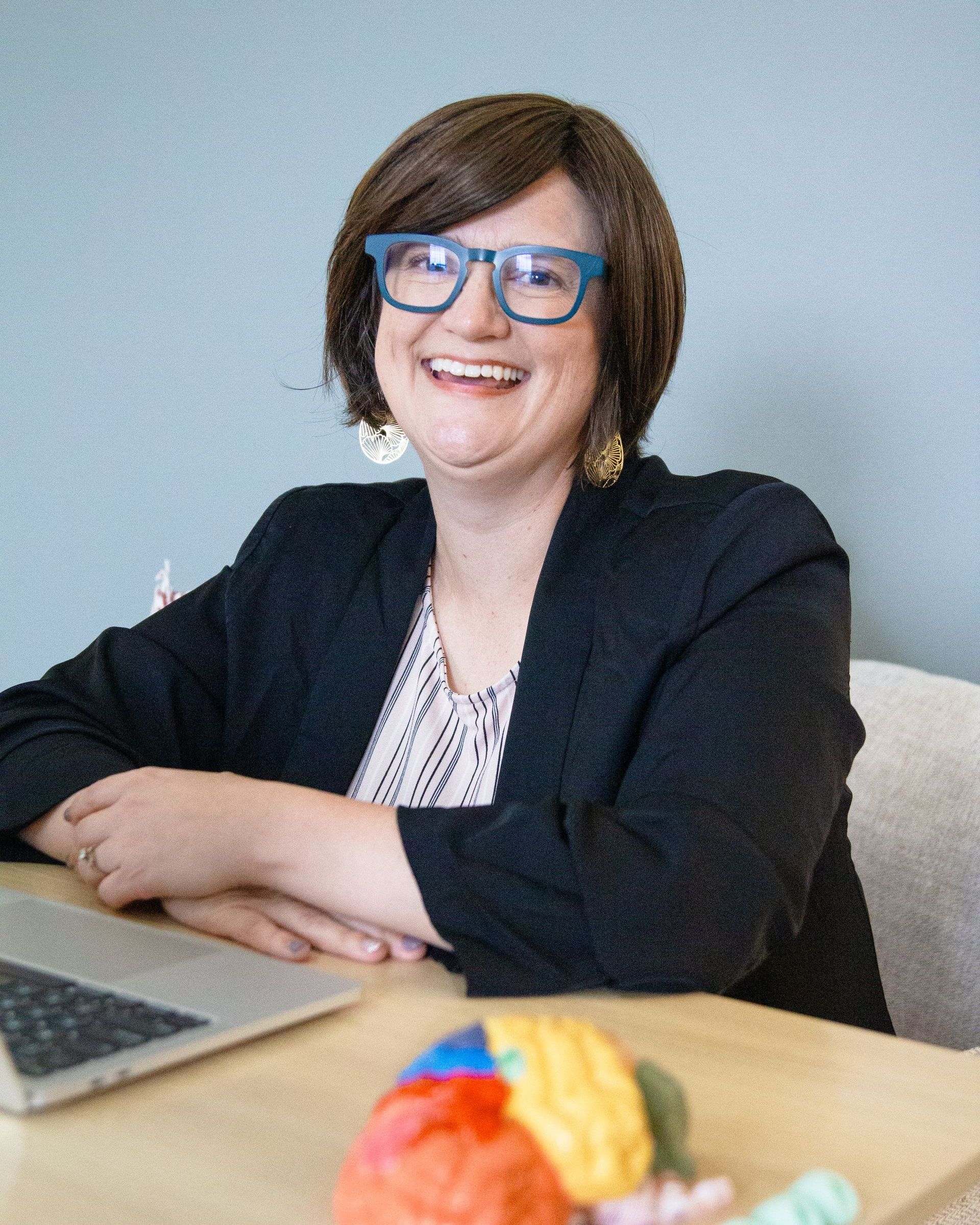 A woman wearing glasses is sitting at a table with a laptop.