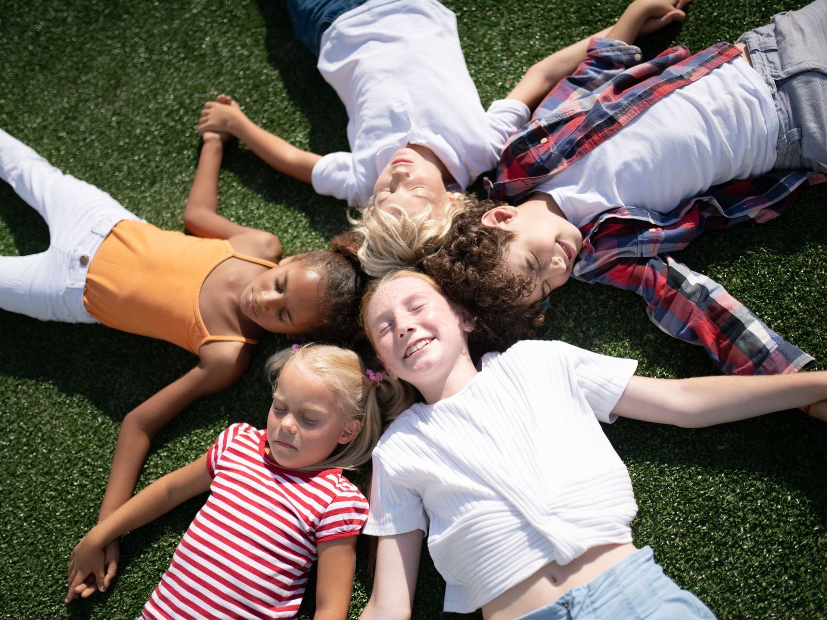 A group of children are laying in a circle on the grass.
