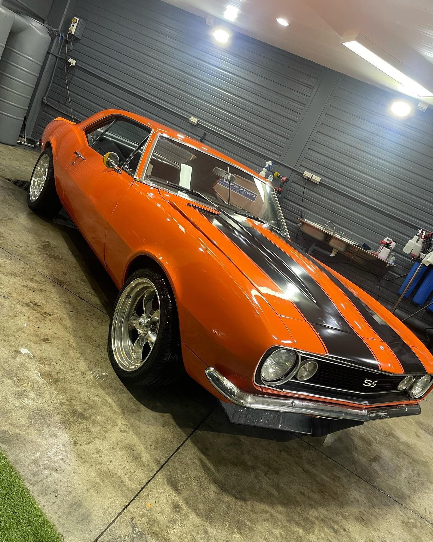 An orange car with black stripes is parked in a garage.