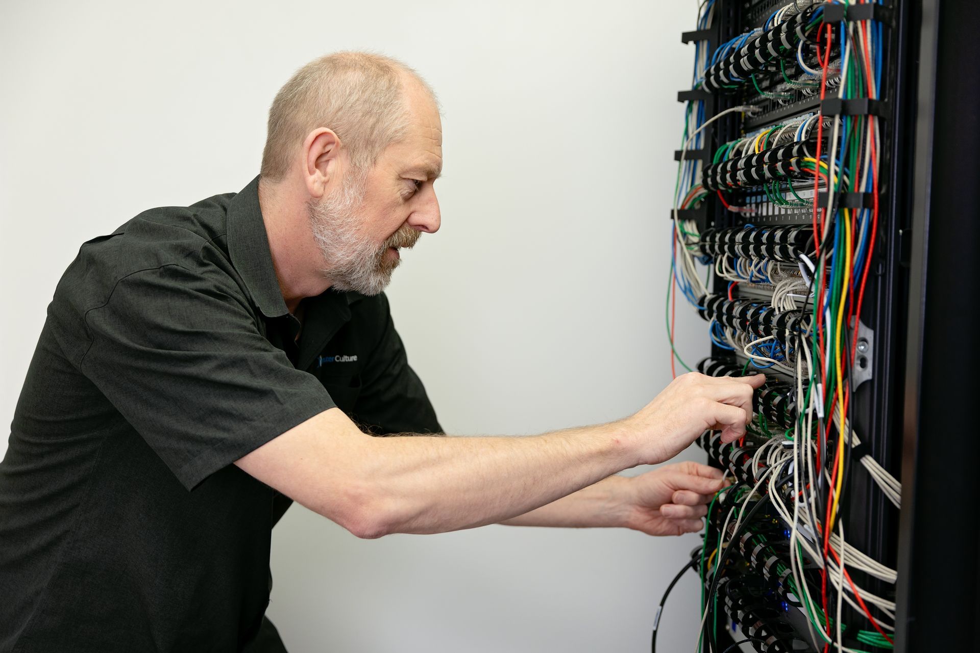 A Computer Culture team member is shifting colourful cables, working on an IT server. 