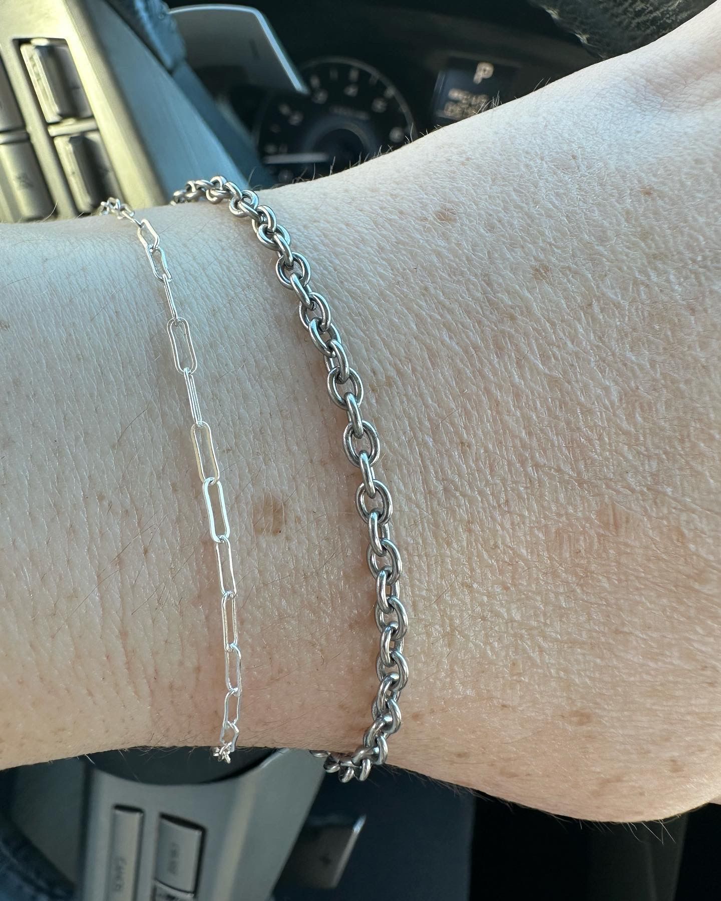 Two silver chain bracelets on a person's wrist.