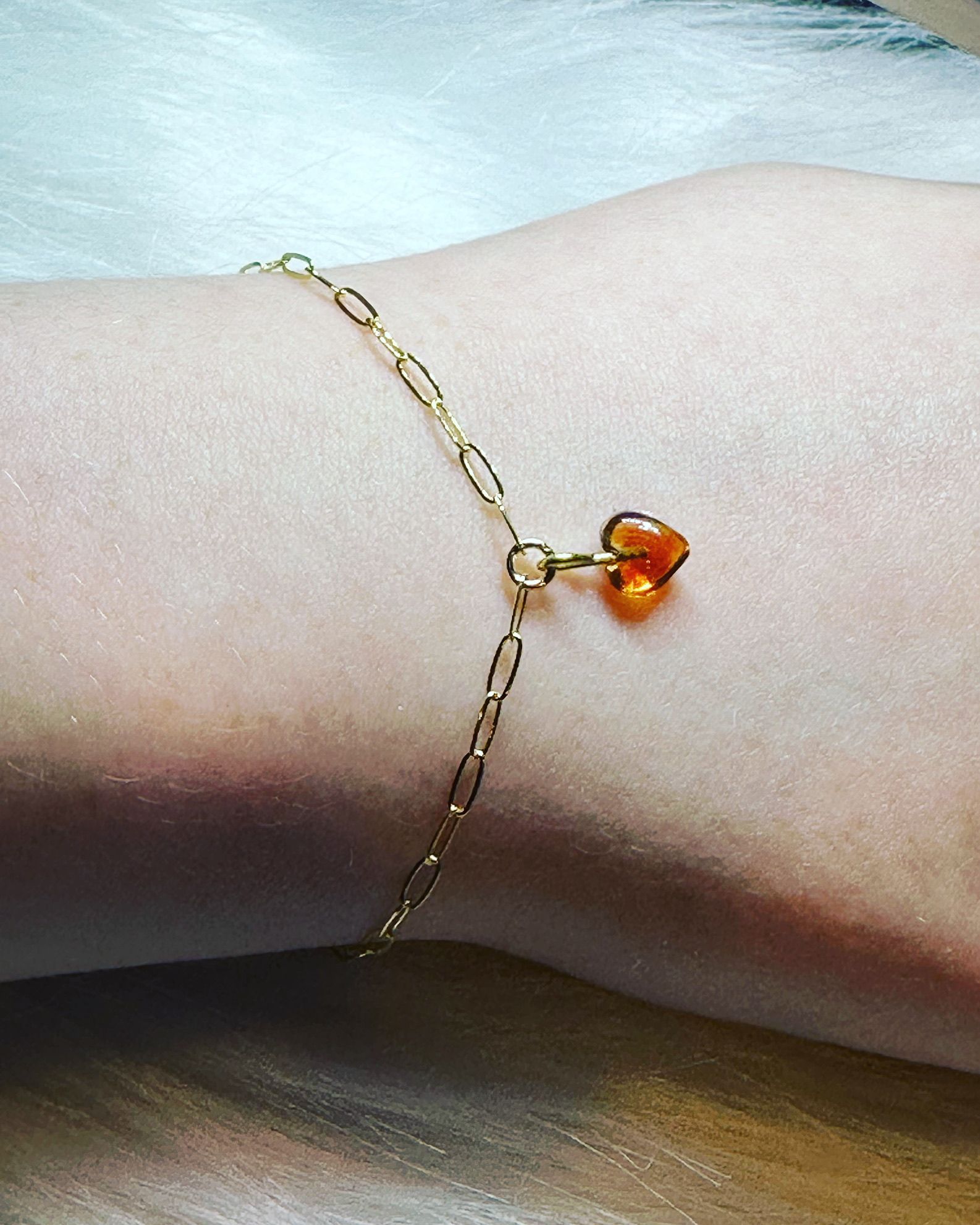 Gold chain bracelet with a heart-shaped orange charm on a wrist.