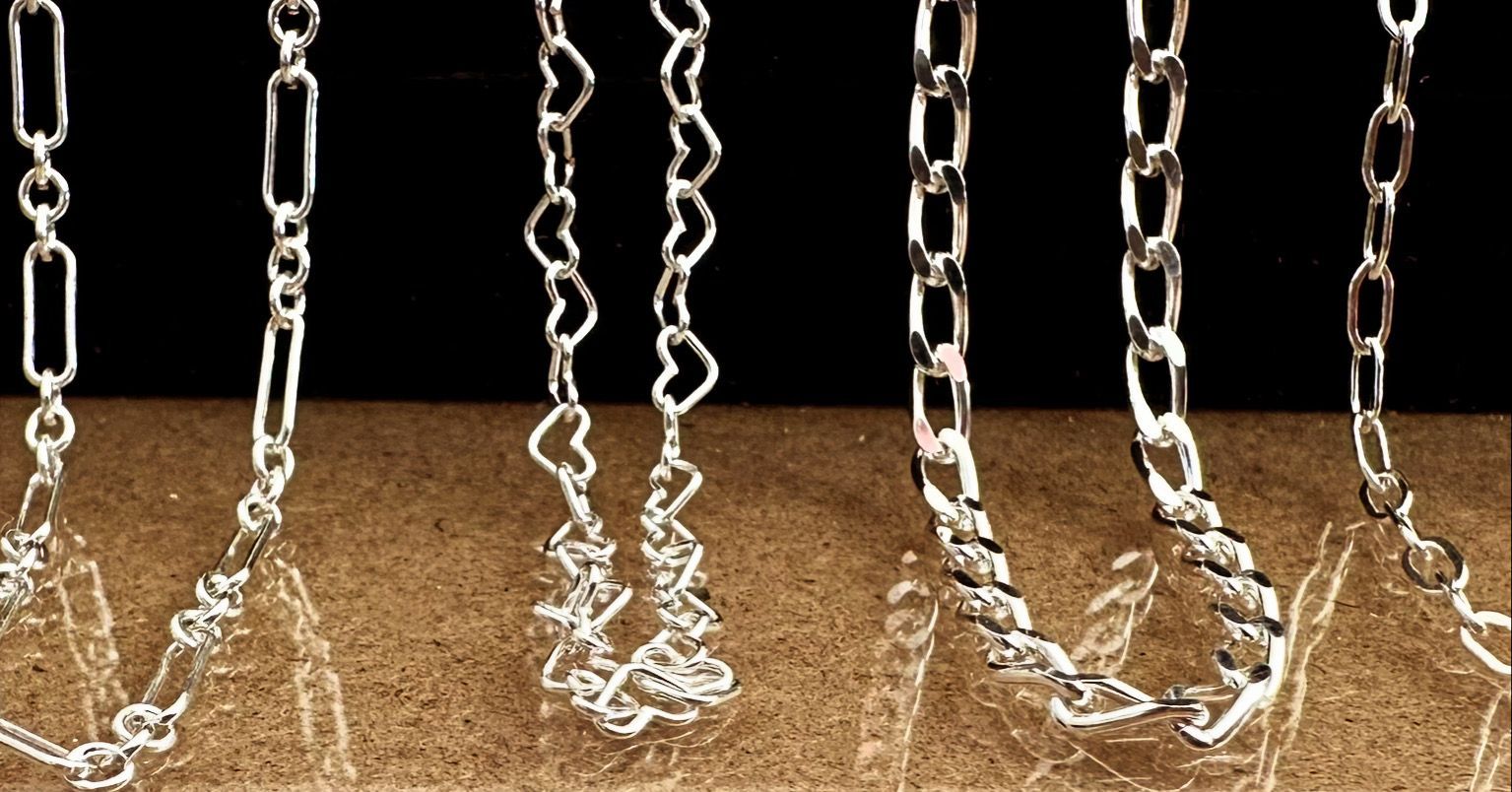 Close-up of six different silver chain styles against a brown surface and black background.